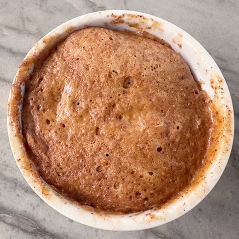 Round white ramekin on gray marble holds amber colored Honey Almond Butter Cake.