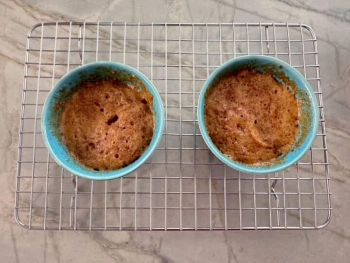 Two blue-green ramekins holding cooked honey almond butter cake sitting on a wire cooling rack.