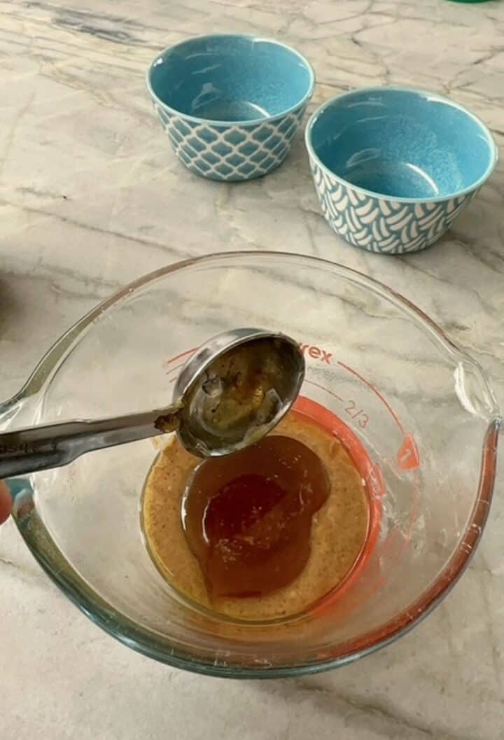 Metal tablespoon adding amber honey to a measuring cup.