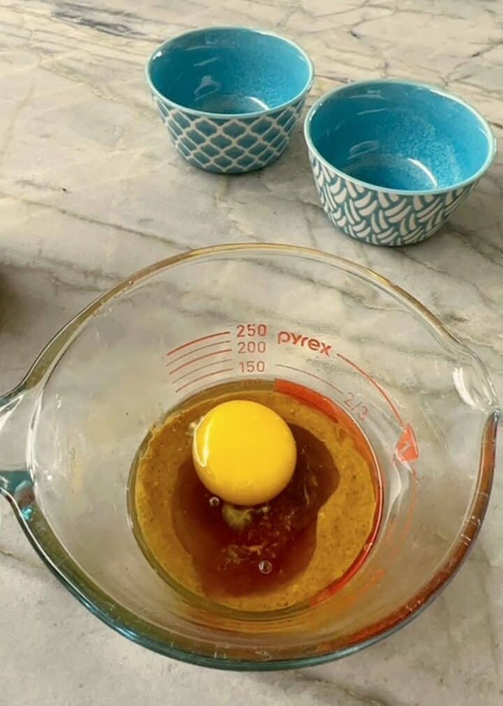 Raw egg floating on top of brown ingredients in a clear measuring cup.