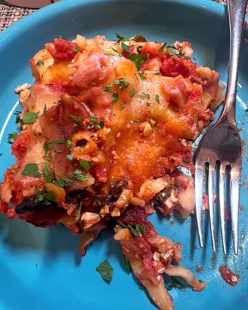 Turquoise blue dish with slice of vegetarian lasagna with glimmers of red tomato sauce and melted cheese.