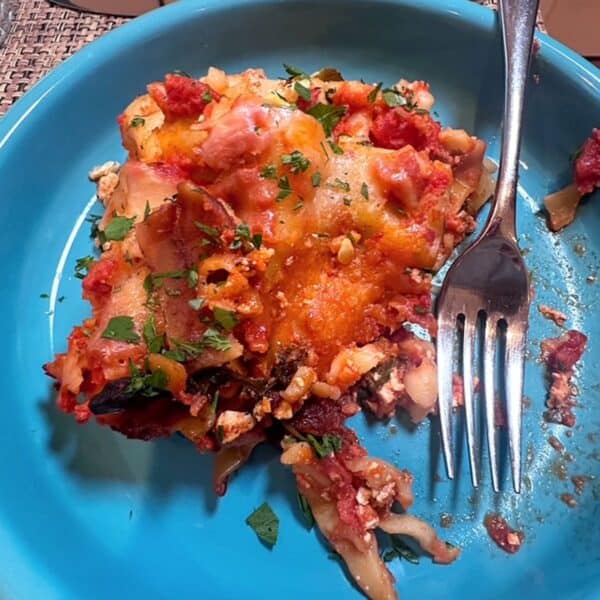 Turquoise blue dish with slice of vegetarian lasagna with glimmers of red tomato sauce and melted cheese.