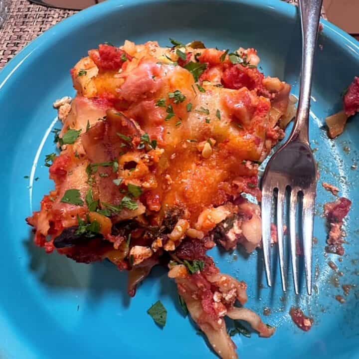 Turquoise blue dish with slice of vegetarian lasagna with glimmers of red tomato sauce and melted cheese.