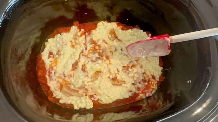 Building a lasagna with red tomato sauce and a layer of white cottage cheese in black liner.