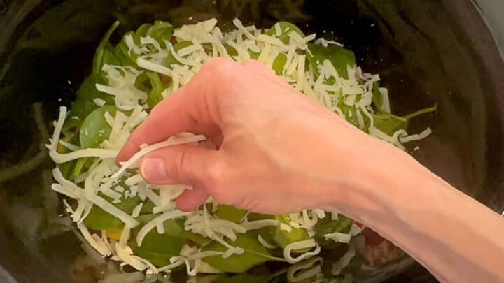 Sprinkling shredded white mozarella cheese over baby spinach to build a Slow Cooker Vegetable Lasagna.
