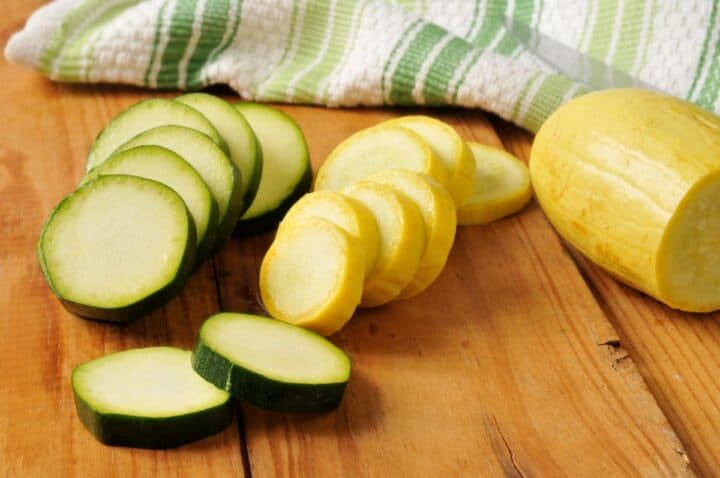 Sliced green zucchini and yellow squash on wooden cutting board.