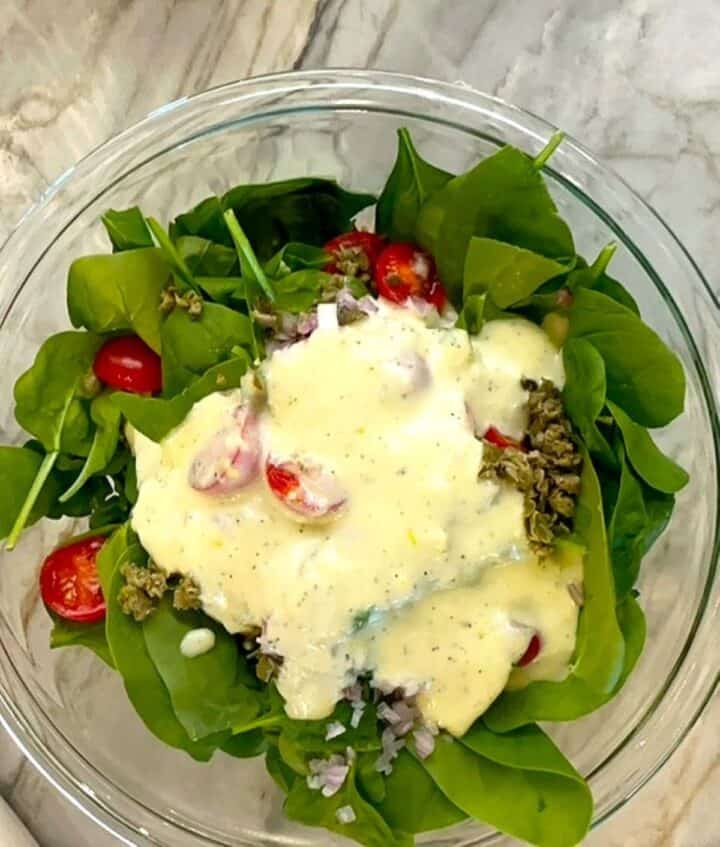 A large splotch of creamy lemon Greek yogurt dressing sits atop green baby spinach salad.