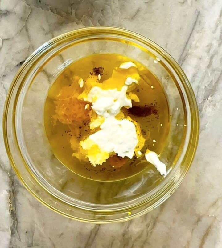 Clear bowl on a gray streaked marble counter holds lemon juice, Greek yogurt and other dressing ingredients.