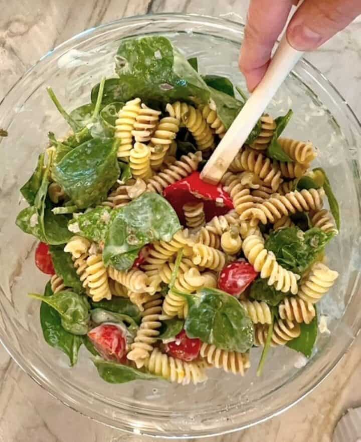 Corkscrew pasta, baby spinach, cherry tomatoes, and more are tossed together with a creamy dressing by a red-headed spaturla.