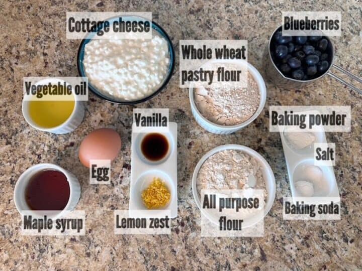 Flours, flavorings, blueberries, oil, cottage cheese, and ingredients needed for blueberry muffins.