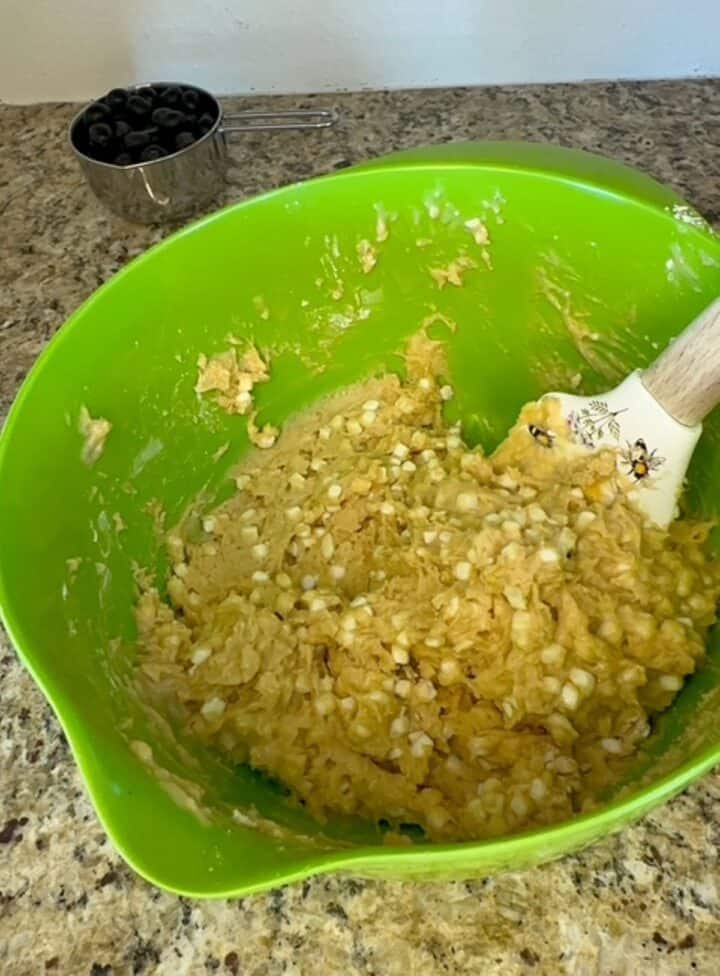 A wooden-handled spatula stirs a thick beige batter studded with white dots of cottage cheese.