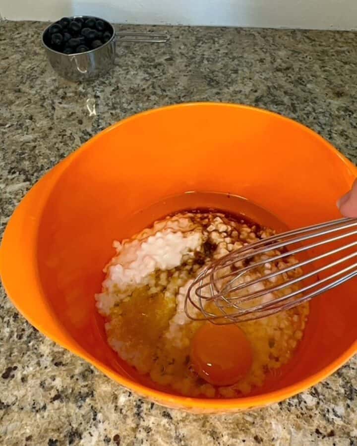 Whisking wet muffin ingredients like an egg, cottage cheese, oil, and more in an orange bowl.