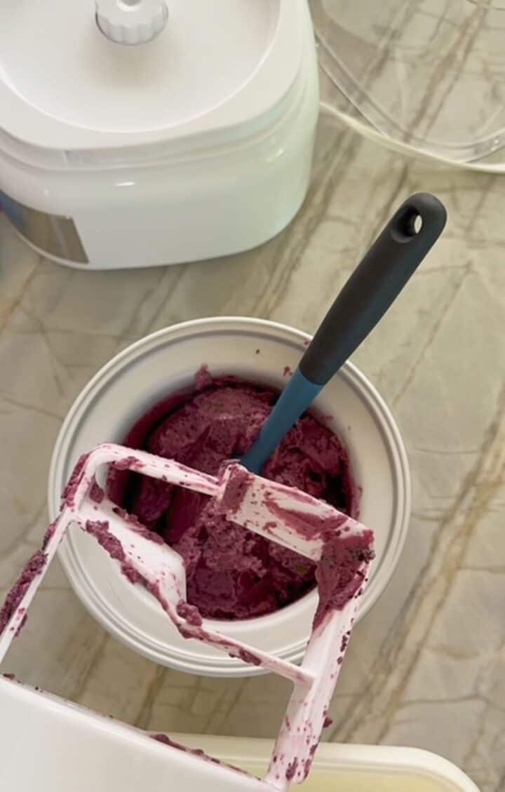 Pulling white paddle out of blueberry Froyo in round, white ice-cream maker bowl.