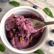 Round white ceramic ramekin filled with purple blueberry yogurt with a spoon dipped into it.