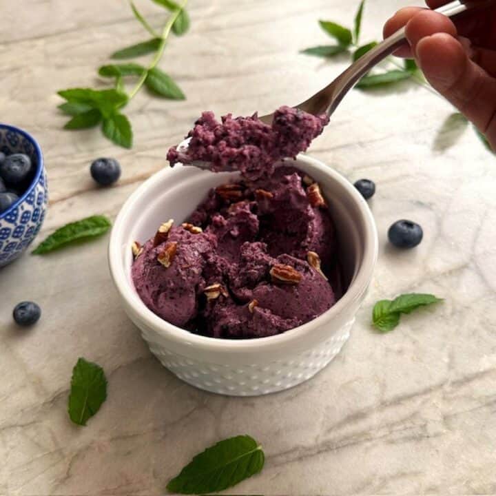 Grabbing a spoonful of purplish frozen blueberry froyo from a round white ramekin that holds a couple of purplish scoops of the dessert.