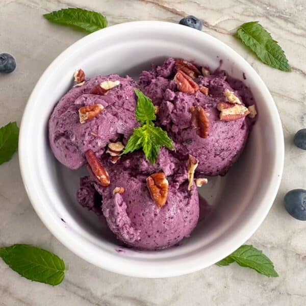 Scoops of purple blueberry frozen yogurt with mint fill a round white ramekin.