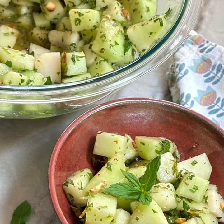 Large clear bowl filled with light green melon cubes flecked with dark green chopped mint.