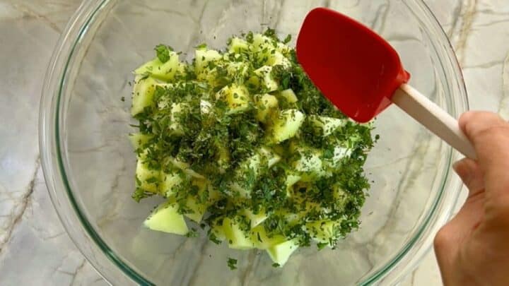 Clear bowl on gray marble countertop full of light green honeydew melon cubes topped with chopped mint.