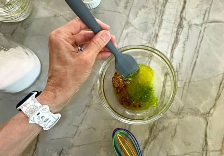 Stirring dressing ingredients of lime juice, zest, olive oil, and spices with a gray spatula.