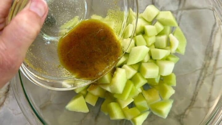 Pouring brownish dressing over light green honeydew cubes in clear bowl.