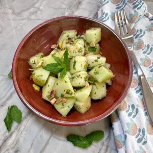 Light green Honeydew melon salad cubes flecked with green bits of mint in a brown bowl with a fork nearby.