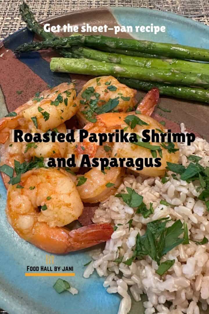 A pile of pink shrimp with green parsley flecks lie on a pottery plate with green asparagus and brown rice.