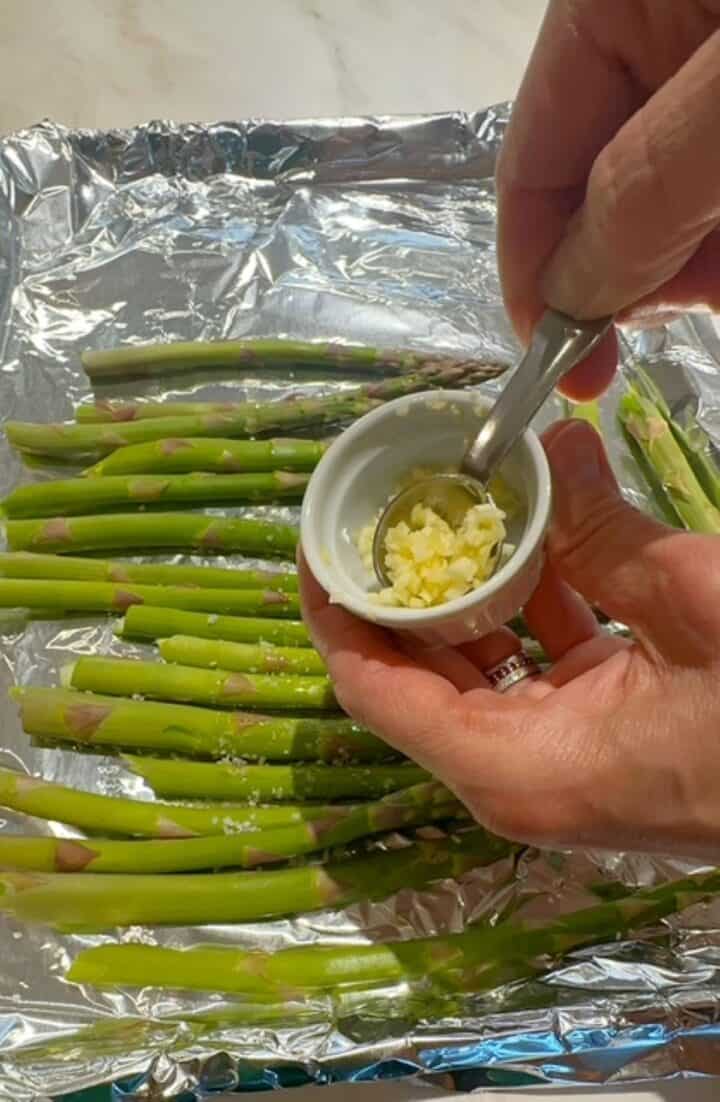 Green asparagus spears glistening with oil on a shiny, foil-lined sheet pan.