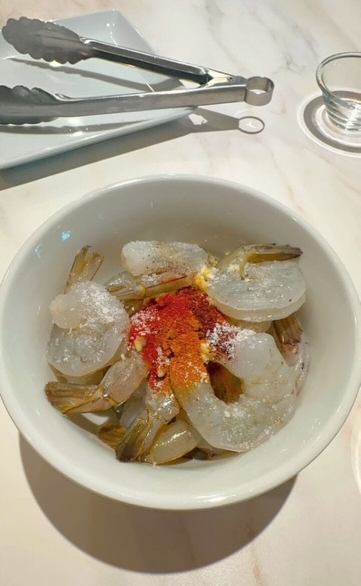 Raw shrimp in white bowl with mound of orange-red seasonings in the center.