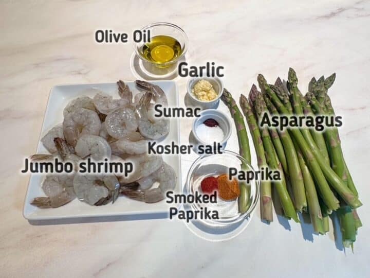 Raw jumbo shrimp, green asparagus spears, olive oil, and seasonings needed and labelled for sheet pan shrimp dinner.