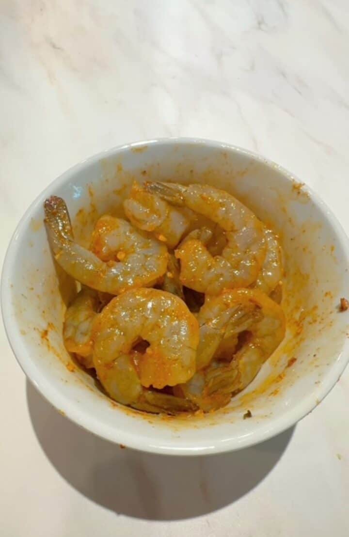 Raw shrimp in white bowl with oil and orange-colored seasonings like paprika.