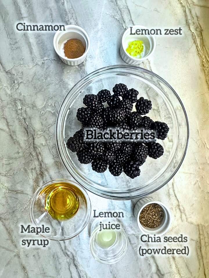 Clear bowl of blackberries surrounded by chia powder and other ingredients for jam.