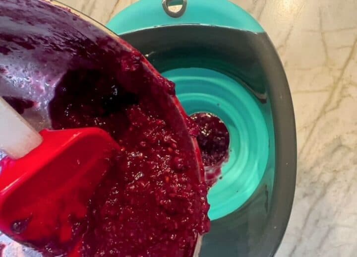 Blackberry mash is poured through a teal and black silicone funnel into a jar.