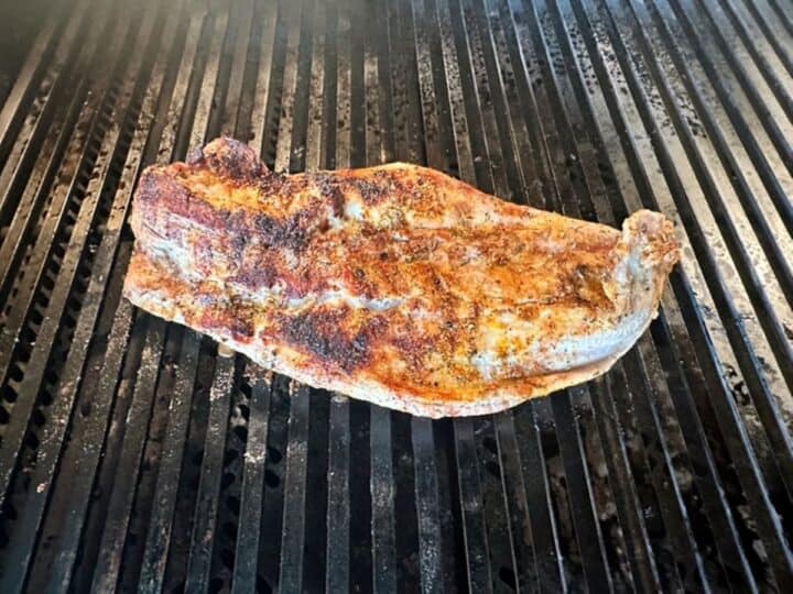 A butterflied pork tender with an appetizing brown crust cooks on a black grill.