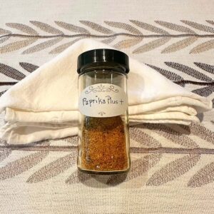 Clear spice jar with reddish paprika spice blend inside on a neutral background.