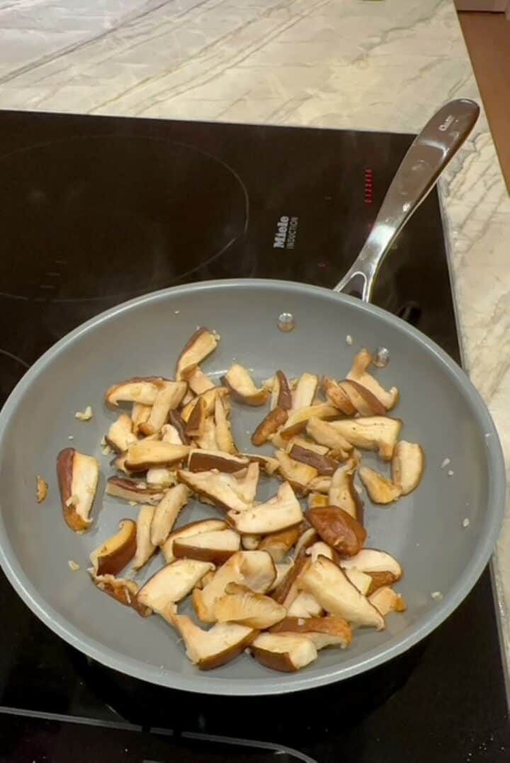 Gray non-stick pan with sliced, cooked brown shiitake mushrooms.