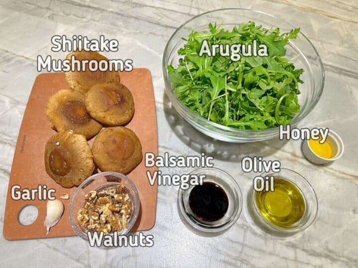 Mound of arugula, round brown shiitake mushrooms and other ingredients for a salad
