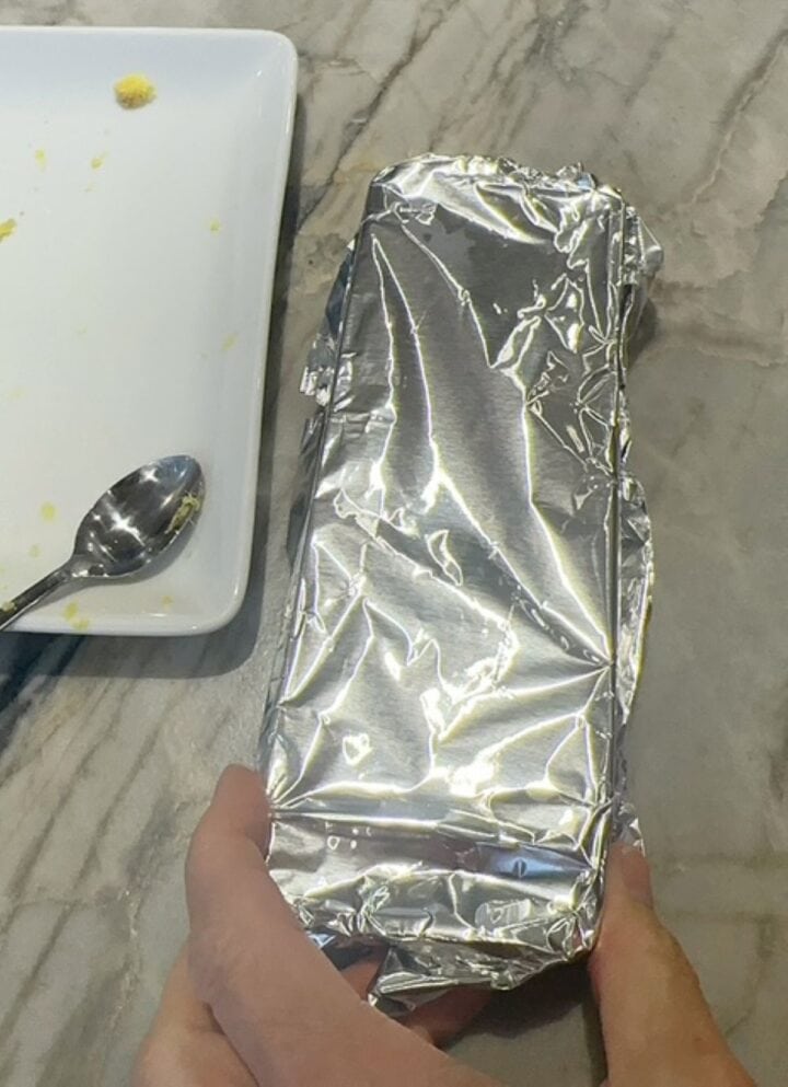 Shiny aluminum foil covers an ice cube tray, forming a seal.