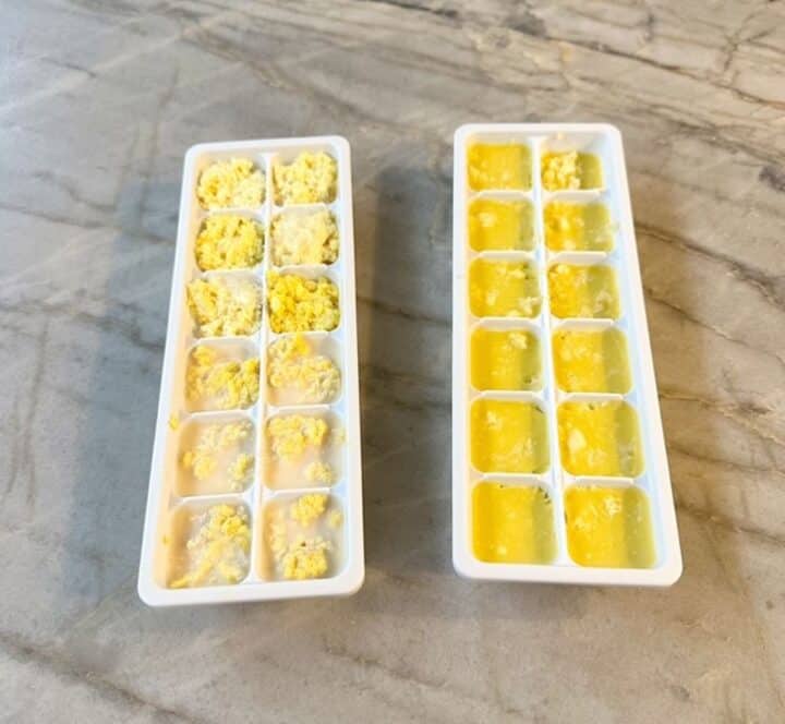 White trays full of golden ,frozen cubes of ginger and garlic on a gray marble countertop.