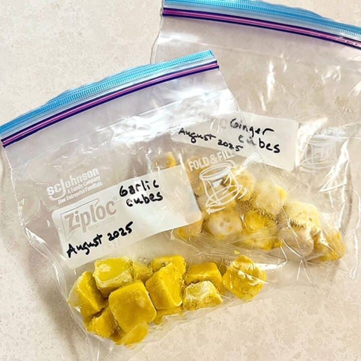 Two clear zip bags filled with golden cubes of ginger and garlic on a white background.