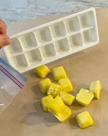 Dumping frozen yellow cubes of garlic out of a white ice cube tray onto brown waxed paper.