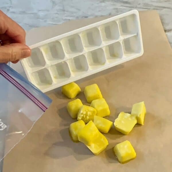 Dumping frozen yellow cubes of garlic out of a white ice cube tray onto brown waxed paper.