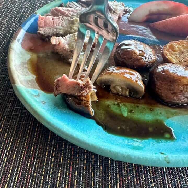 A fork holds together a bite of red-brown rare steak with a piece of juicy mushroom.