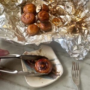 Tongs remove a whole mushroom from crumpled, stained foil to a small squarish plate.