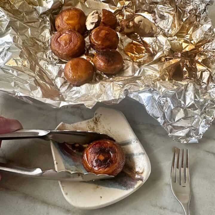 Tongs remove a whole mushroom from crumpled, stained foil to a small squarish plate.