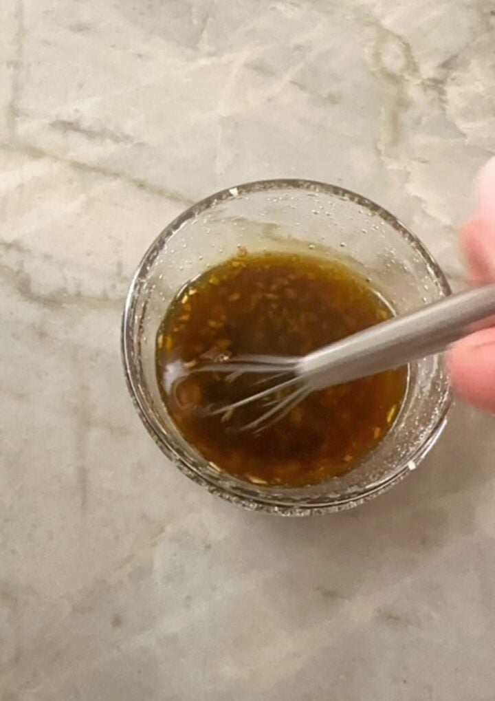 Small, clear bowl contains a whisk in a thick mix of brown-green balsamic and olive oil.
