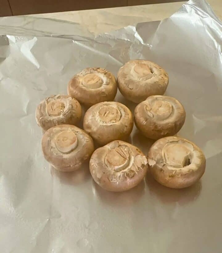 Several light brown baby Bella mushrooms on a square of shiny aluminum foil.