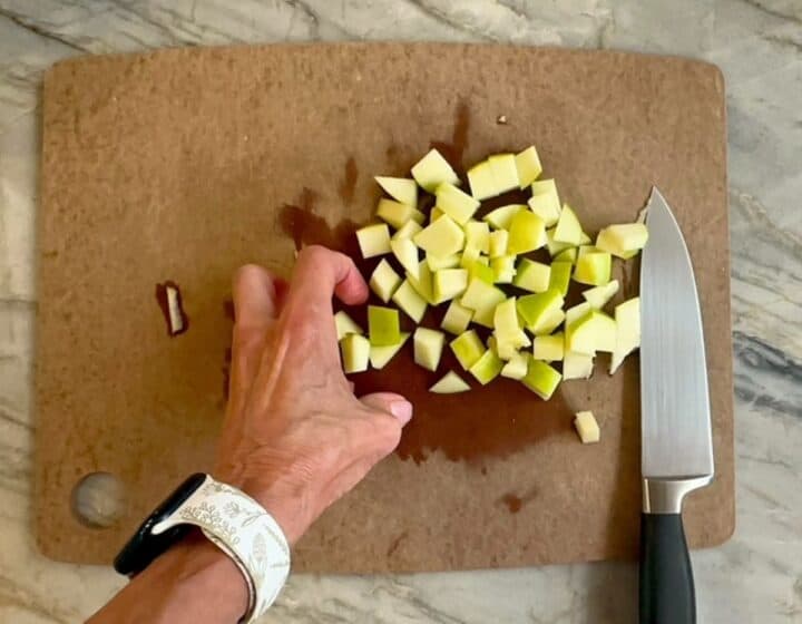 Small cubes of green apple on a brown cutting board with a silver chef's knife.
