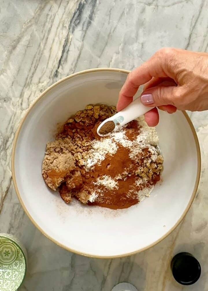 Light brown granola with white flour, brown sugar, cinnamon, etc in a white bowl.
