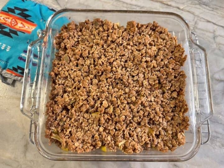 Baked brown apple crisp with granola topping in square clear baking dish.