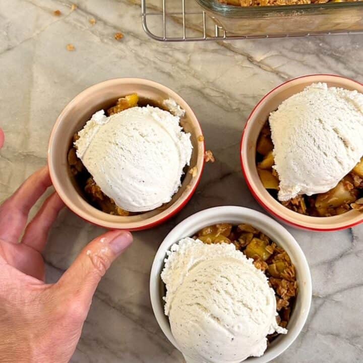Three round dishes hold apple crisp topped with a white scoop of vanilla ice cream.